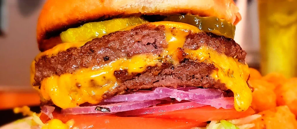 Double cheeseburger with melted cheese, brioche bun, pickles, and fresh vegetables.
