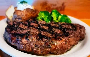 Grilled steak, baked potato, and steamed broccoli on a white plate.