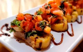 Plate of bruschetta with tomatoes, basil, and balsamic drizzle.