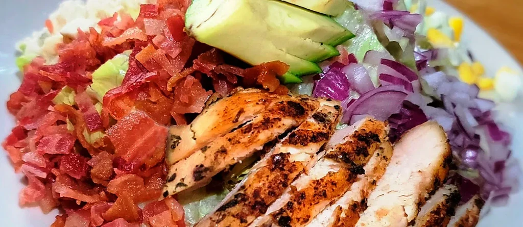 Vibrant salad with grilled chicken, bacon, avocado, corn, and red onion.