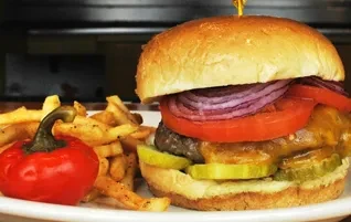 Fully dressed cheeseburger, golden fries, and red pepper on a white plate.
