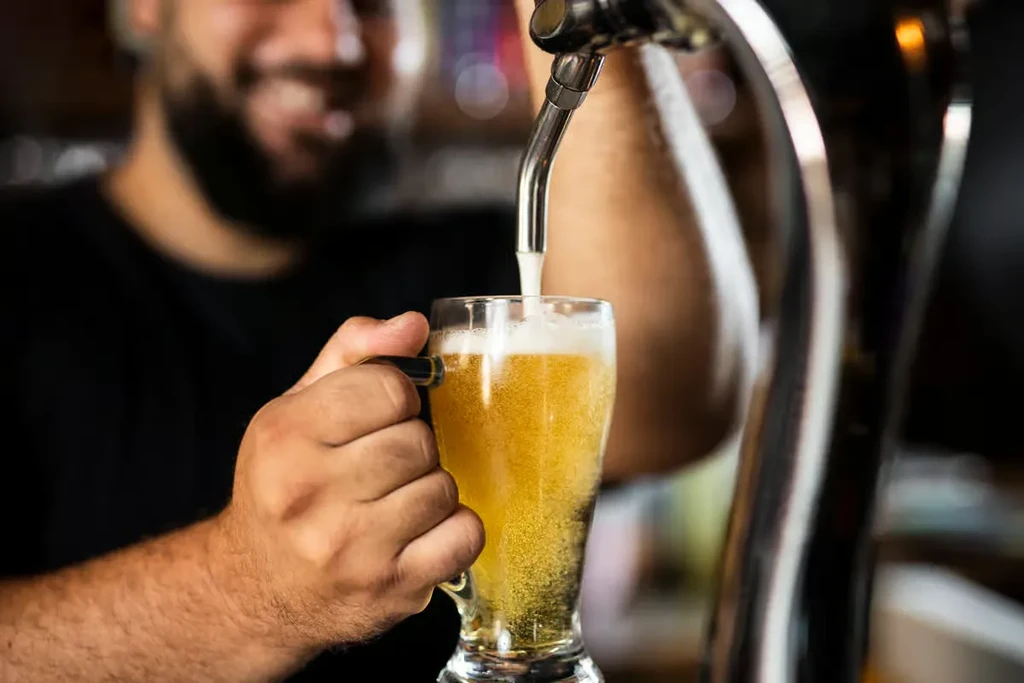 Golden beer pours from silver tap into a clear glass mug.