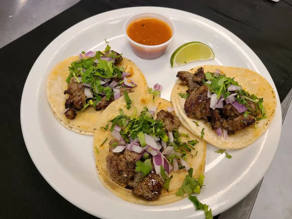 Three meat tacos with onion, cilantro, salsa, and lime.