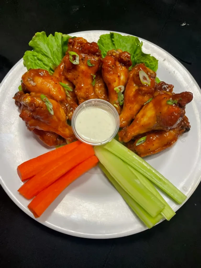 Buffalo chicken wings, dip, carrots, and celery on a white plate.