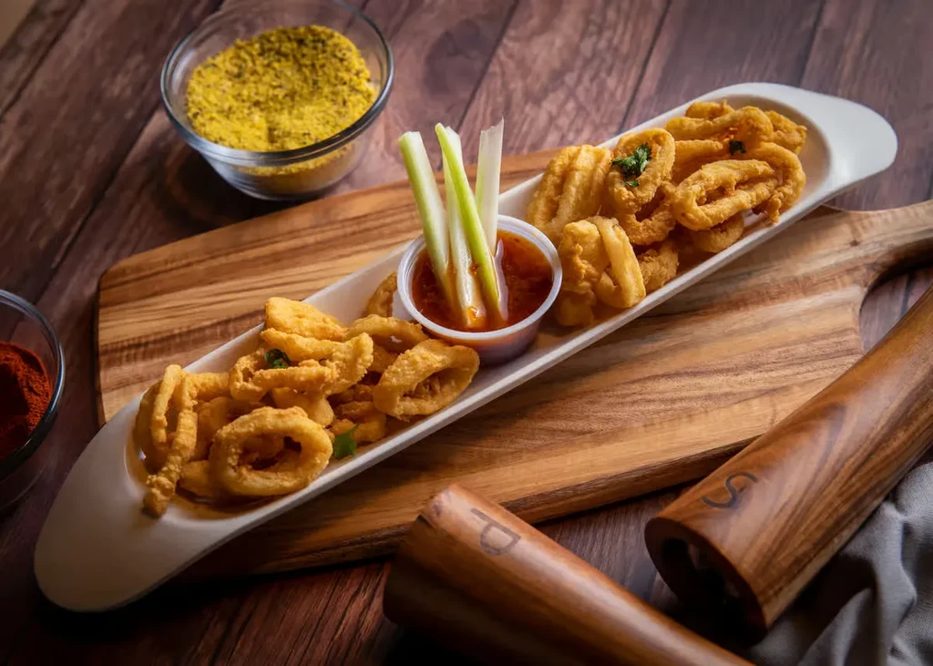 Platter of crispy fried calamari, sauce, spices, and grinders on wood.