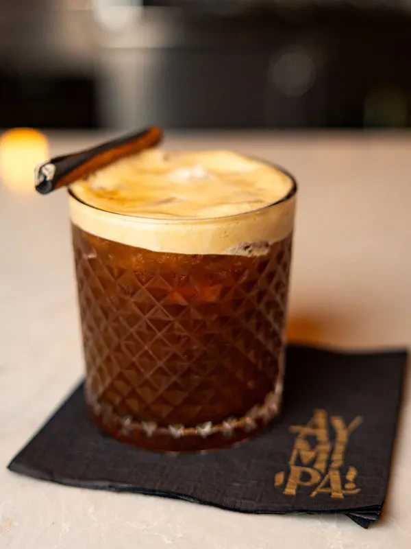 Close-up of a faceted cocktail with creamy foam and dark garnish.