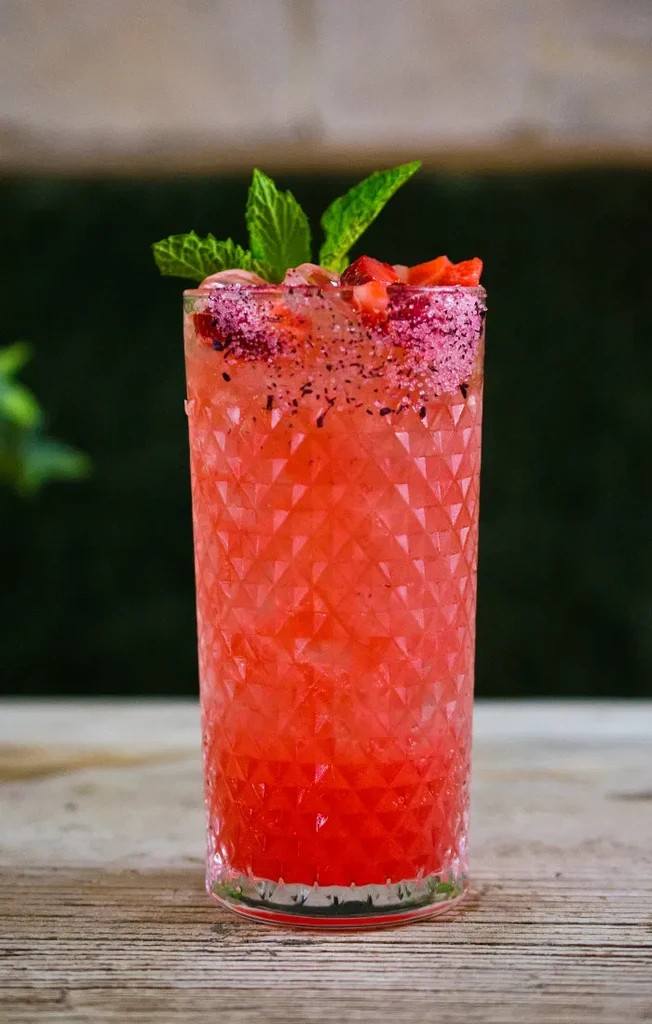 Red-orange drink with crushed ice, red fruit, mint, and sugar rim.