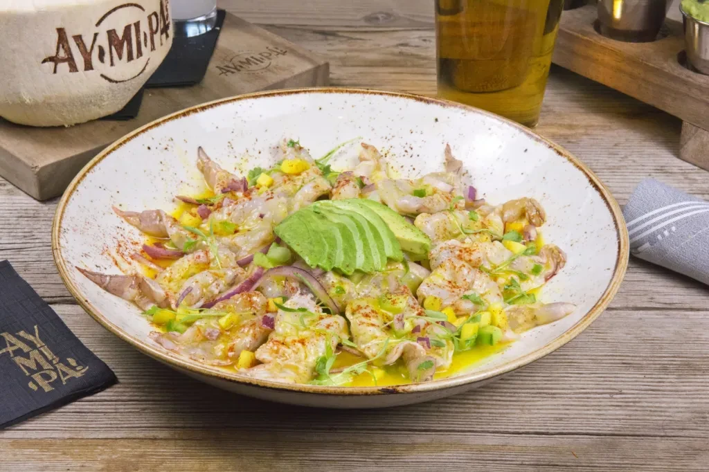 Shrimp ceviche with avocado, red onion, and herbs on a wooden table.