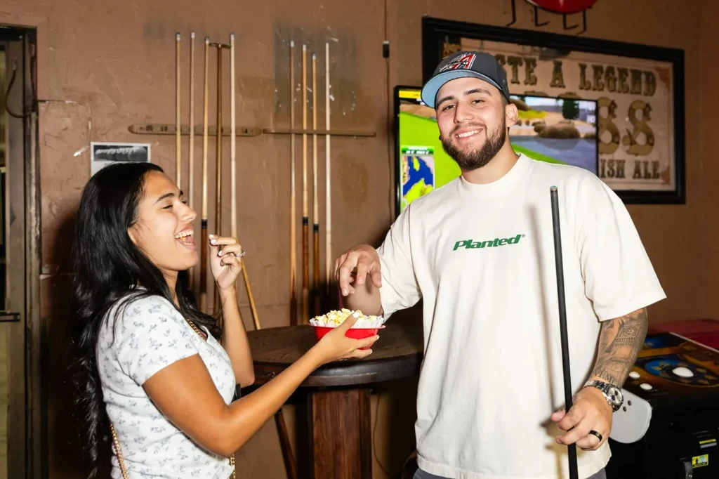 Man takes popcorn from a laughing woman in a billiards bar.