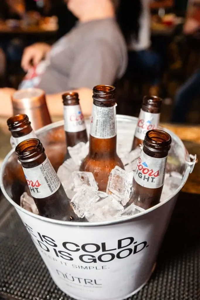 White metal bucket filled with ice and cold Coors Light bottles.
