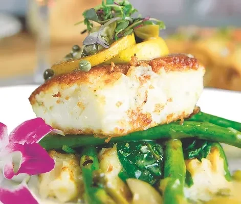 Plated white fish fillet with asparagus, creamy puree, lemon, and orchid.