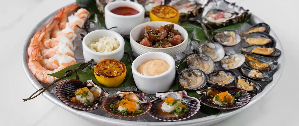 Platter of shrimp, oysters, clams, mussels, scallops, and poke on ice.