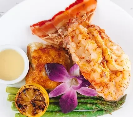 Seafood plate with grilled lobster, asparagus, charred lemon, and purple orchid.