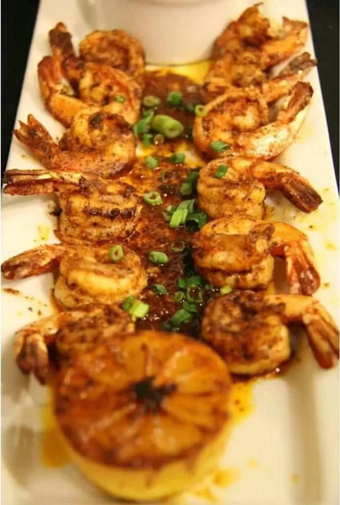Pan-seared shrimp with sauce, green onions, and roasted lemon on a plate.