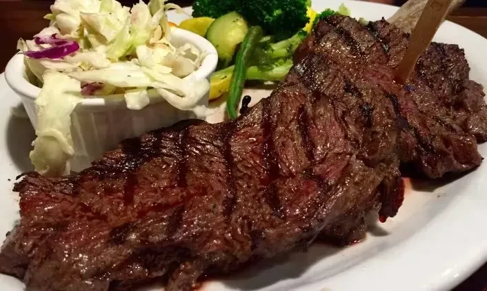 Grilled medium-rare steak served with vegetables and coleslaw.