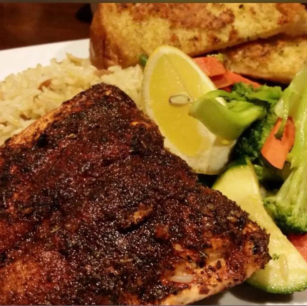Blackened fish, brown rice, steamed vegetables, lemon, and garlic bread.