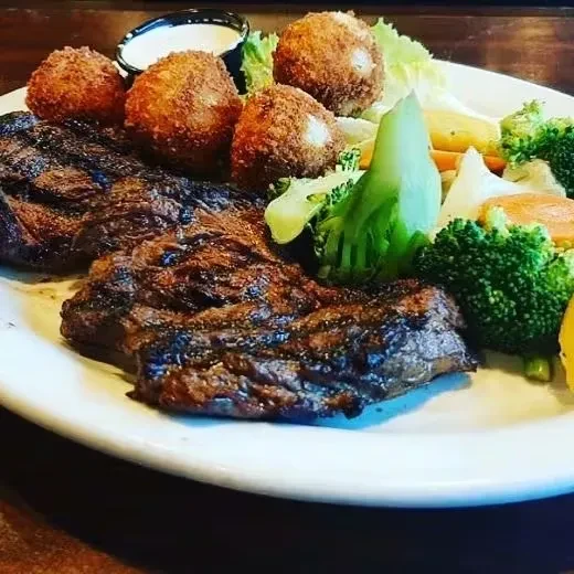 Grilled steak, croquettes, and vegetables with dipping sauce on a plate.