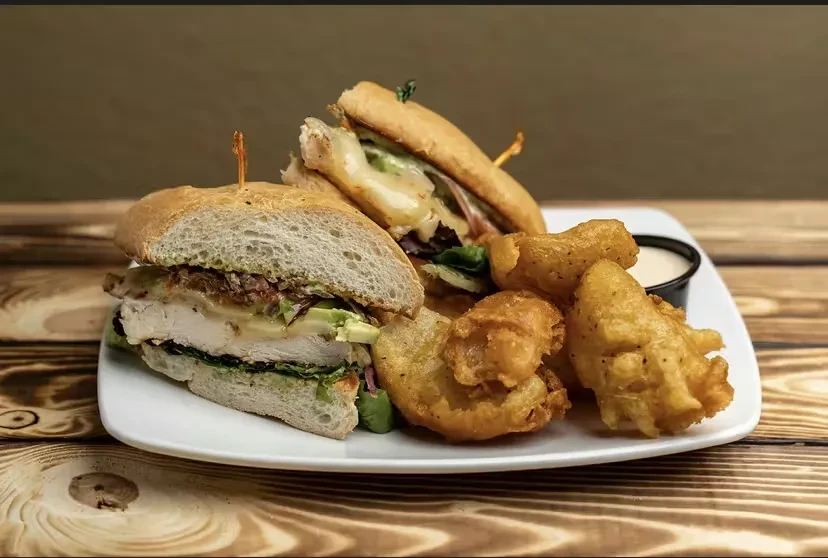 Two sub sandwich halves, crispy fried food, and sauce on wood.