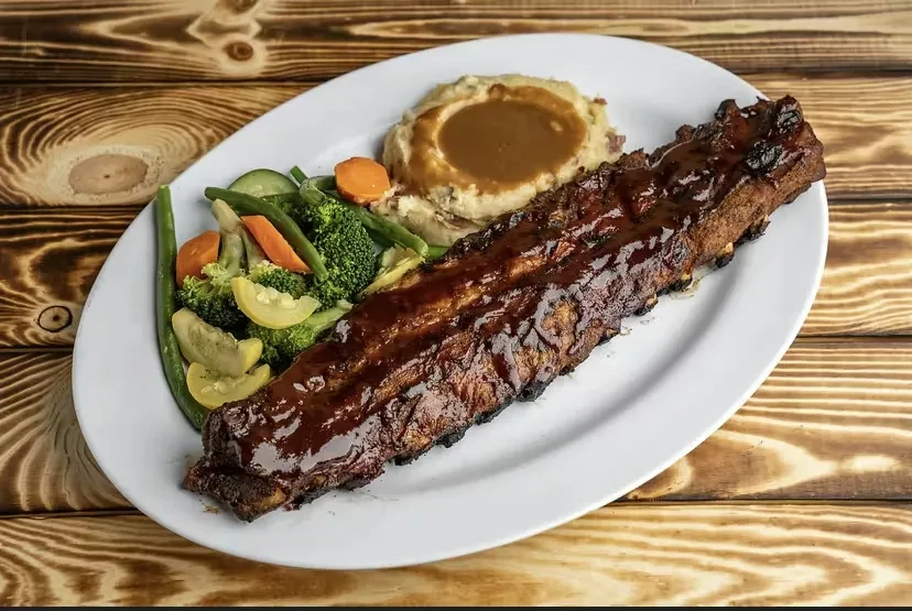 Glistening BBQ ribs, mashed potatoes with gravy, and colorful steamed vegetables.