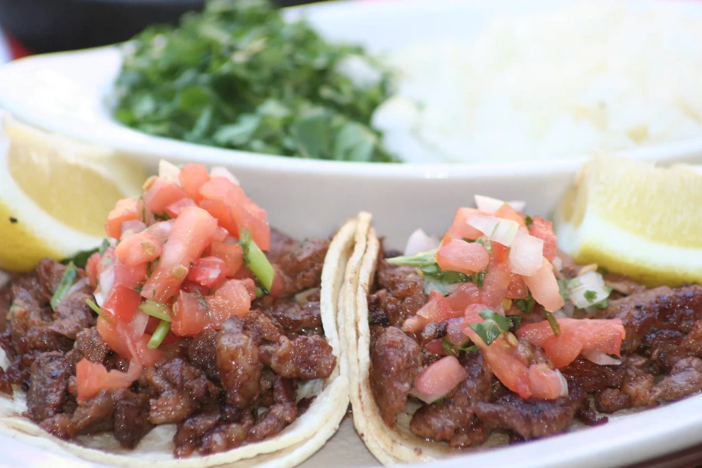 Close-up of two meat tacos with pico de gallo and lime wedges.