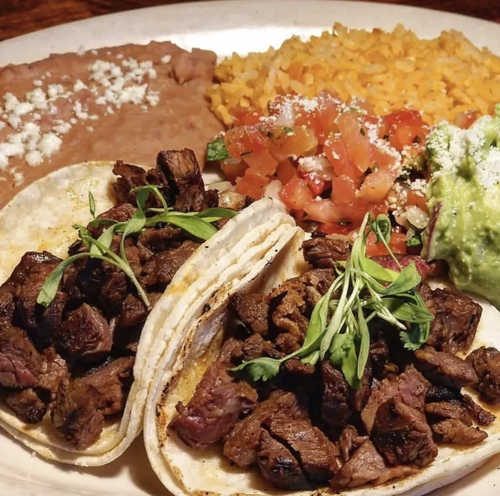 Two meat tacos with refried beans, rice, pico de gallo, and guacamole.