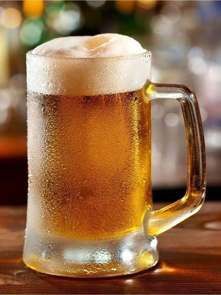 Frosty mug of amber beer with thick foam and condensation.