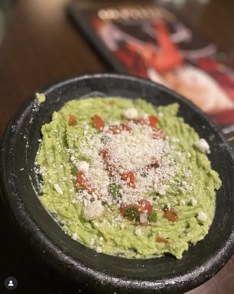 Rustic bowl of guacamole topped with cheese, diced tomatoes, and herbs.