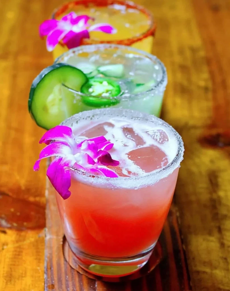 Three vibrant cocktails with unique garnishes on rustic wood.