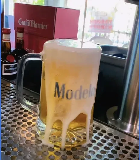 Modelo beer mug overflowing with foam on a bar tray.