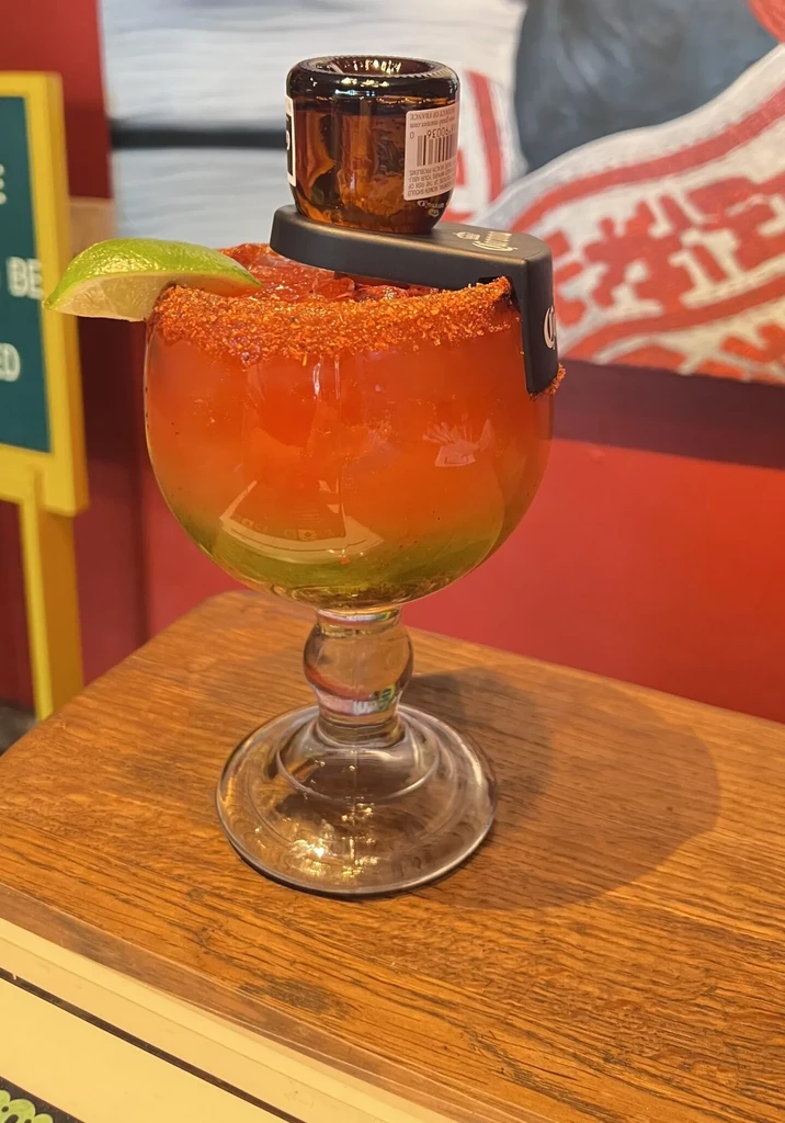Elaborate reddish-orange drink, green layer, seasoned rim, lime, and inverted bottle.