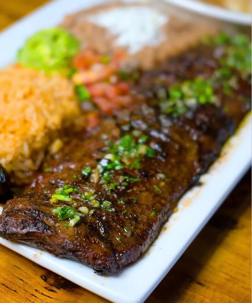 Close-up of grilled skirt steak, orange rice, beans, and guacamole.