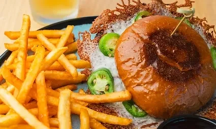 Gourmet burger with jalapeños, cheese tuile, and golden french fries.