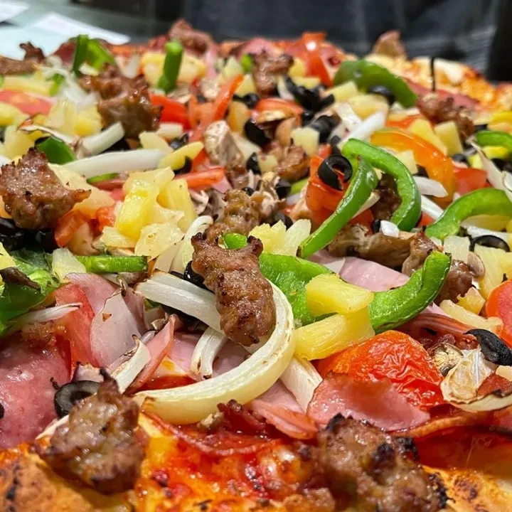 Fully-loaded pizza close-up, featuring meats, vegetables, olives, mushrooms, and pineapple.