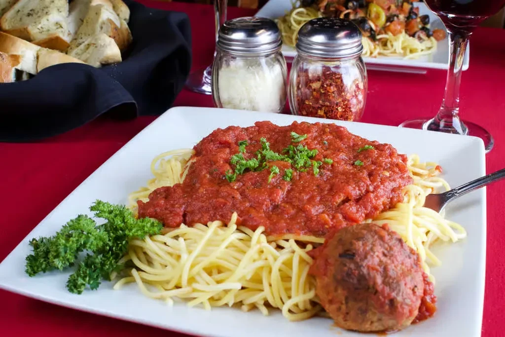 Spaghetti and meatball with garlic bread on a red tablecloth.
