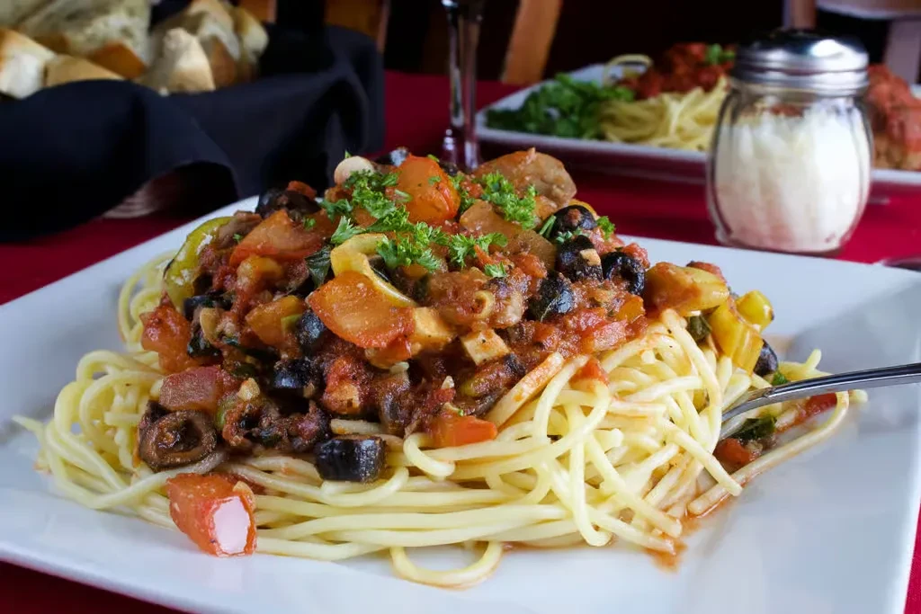 Close-up of spaghetti with chunky tomato sauce, olives, and bell peppers.