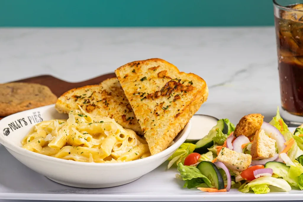 Tray with penne pasta, garlic bread, side salad, drink, and cookie.