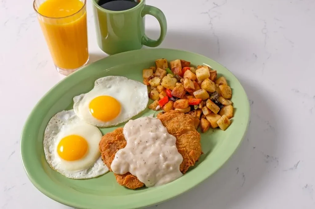 Sunny-side-up eggs, gravy-covered fried chicken, home fries, juice, and coffee.