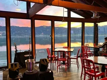 Restaurant with red chairs, stage, and panoramic sunset view over water.
