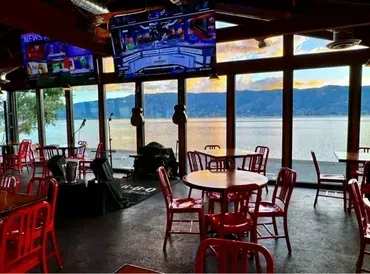 Restaurant interior with red chairs, industrial ceiling, and water view.