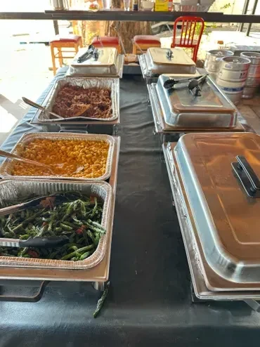 Buffet table of shredded meat, mac and cheese, green beans outdoors.