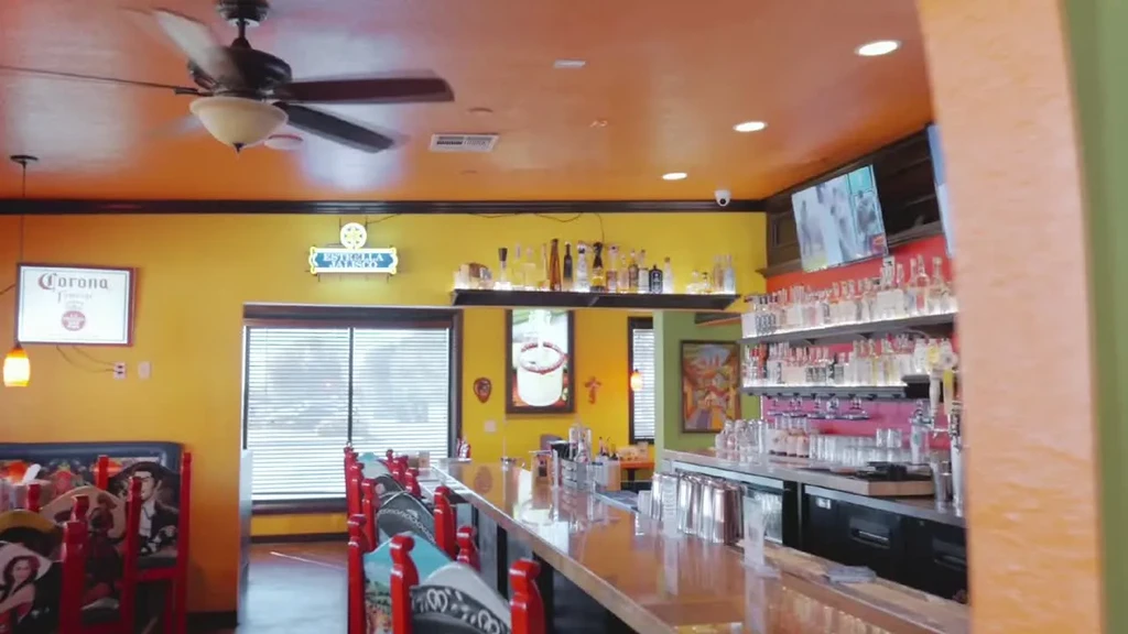 Mexican-themed bar interior with colorful walls, liquor bottles, and character stools.