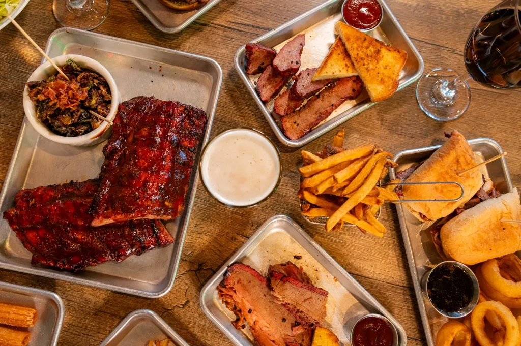 Rustic table with barbecue ribs, brisket, fries, sprouts, beer and wine.
