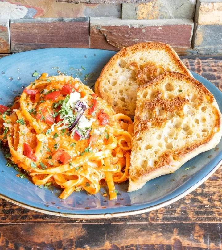 Pasta with orange sauce, tomatoes, green herbs, and toasted bread.