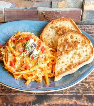 Creamy pasta, tomatoes, herbs, and toasted bread on a blue plate.