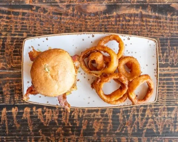 Burger with bacon and golden onion rings on a wooden table.