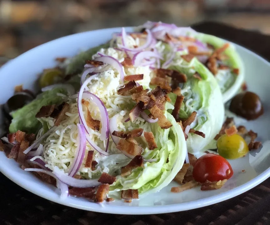 Wedge salad with cheese, bacon, red onion, cherry tomatoes, and creamy dressing.