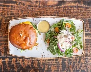 White plate with a sandwich, creamy sauce, and arugula salad.