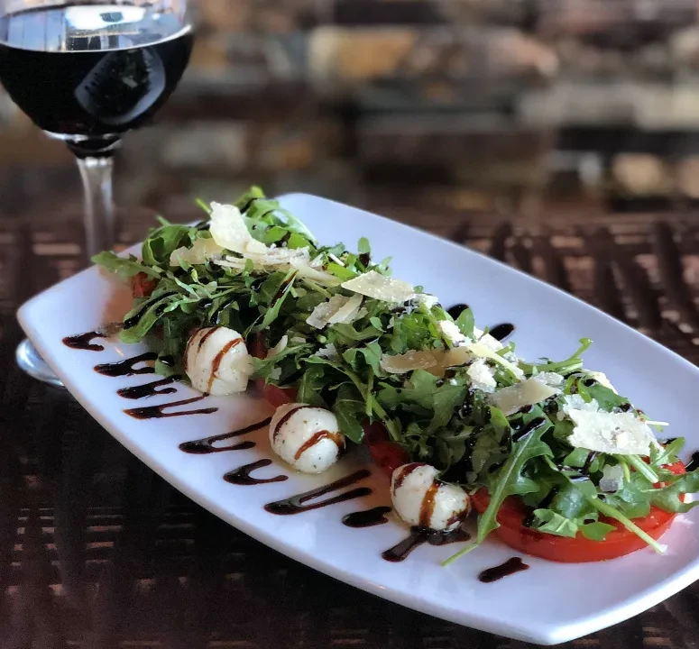 Caprese salad with tomatoes, mozzarella, arugula, Parmesan, and red wine.