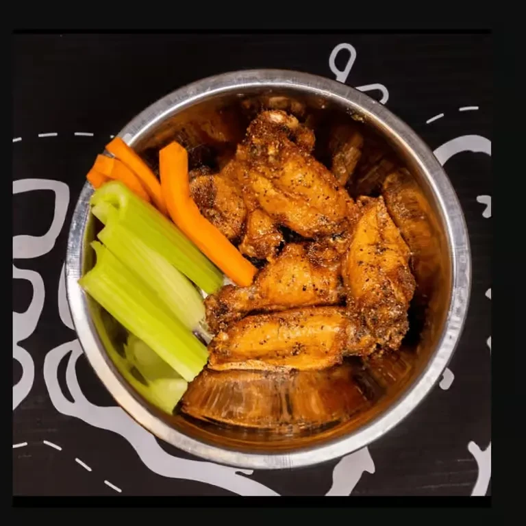Golden-brown chicken wings with celery and carrot sticks in a steel bowl.