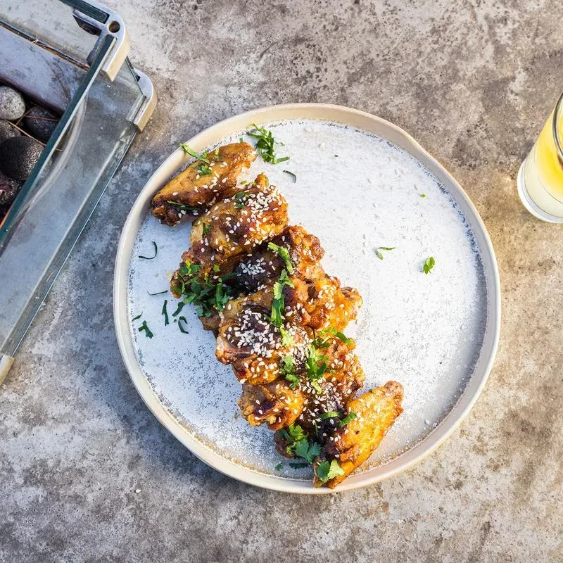 Glazed chicken wings with sesame seeds and green herbs on a plate.